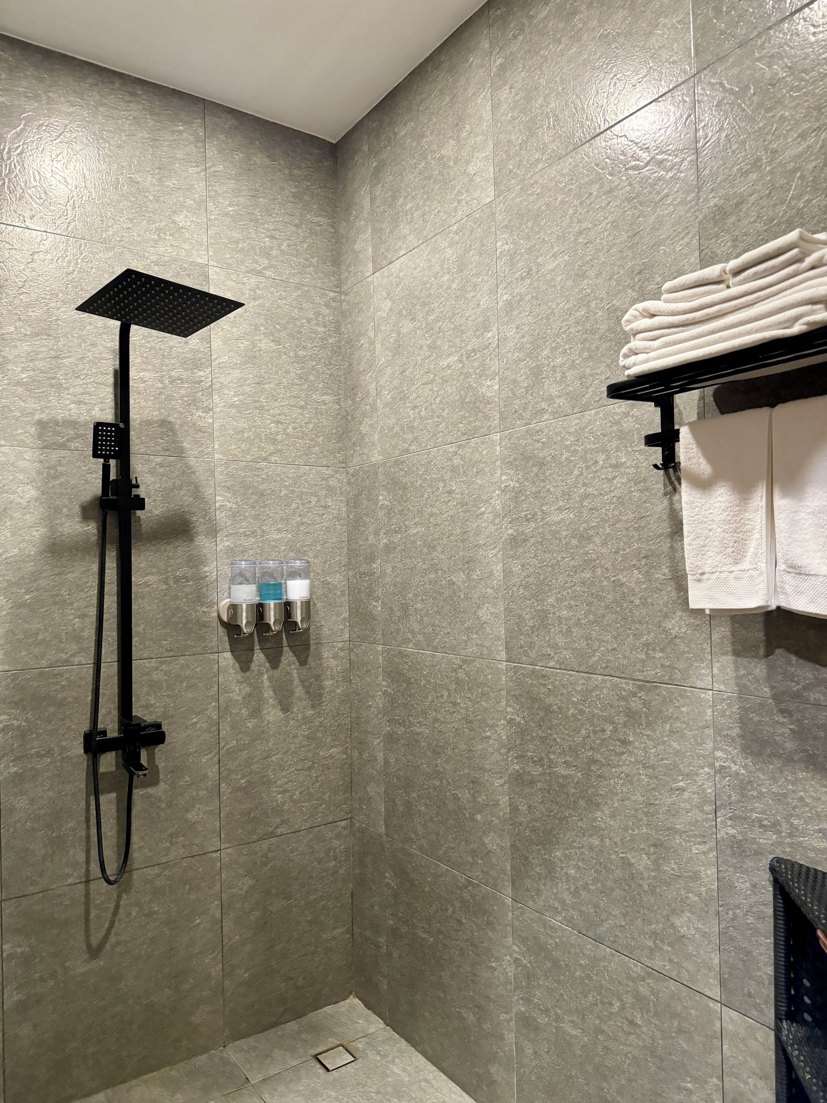 Un área de ducha con ducha de techo cuadrada, ducha de mano y dispensador de jabón.