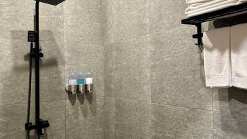 Un área de ducha con ducha de techo cuadrada, ducha de mano y dispensador de jabón.