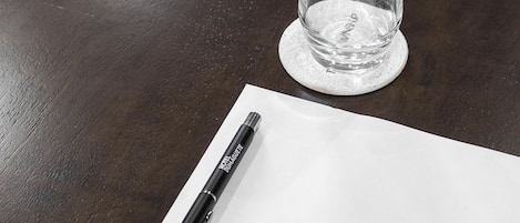 A clear glass on a coaster, a pen on a white paper, and a dark wooden table.