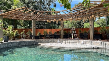 A swimming pool with a wooden pergola overhead, surrounded by outdoor furniture and plants.