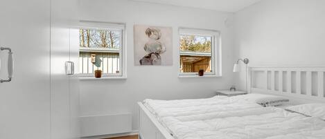 A bedroom with a large bed, two windows, a ceiling light, and a small bedside table.