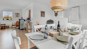 Een eetruimte met een witte tafel voor vier personen, een hanglamp en een keuken op de achtergrond.