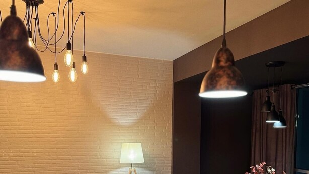 A modern living room with a brick wall, a wooden coffee table with a 'Merry Christmas' placemat, a lamp, and a TV on a black stand. - Middle Asia Deer Cave in Urban City (Almaty)