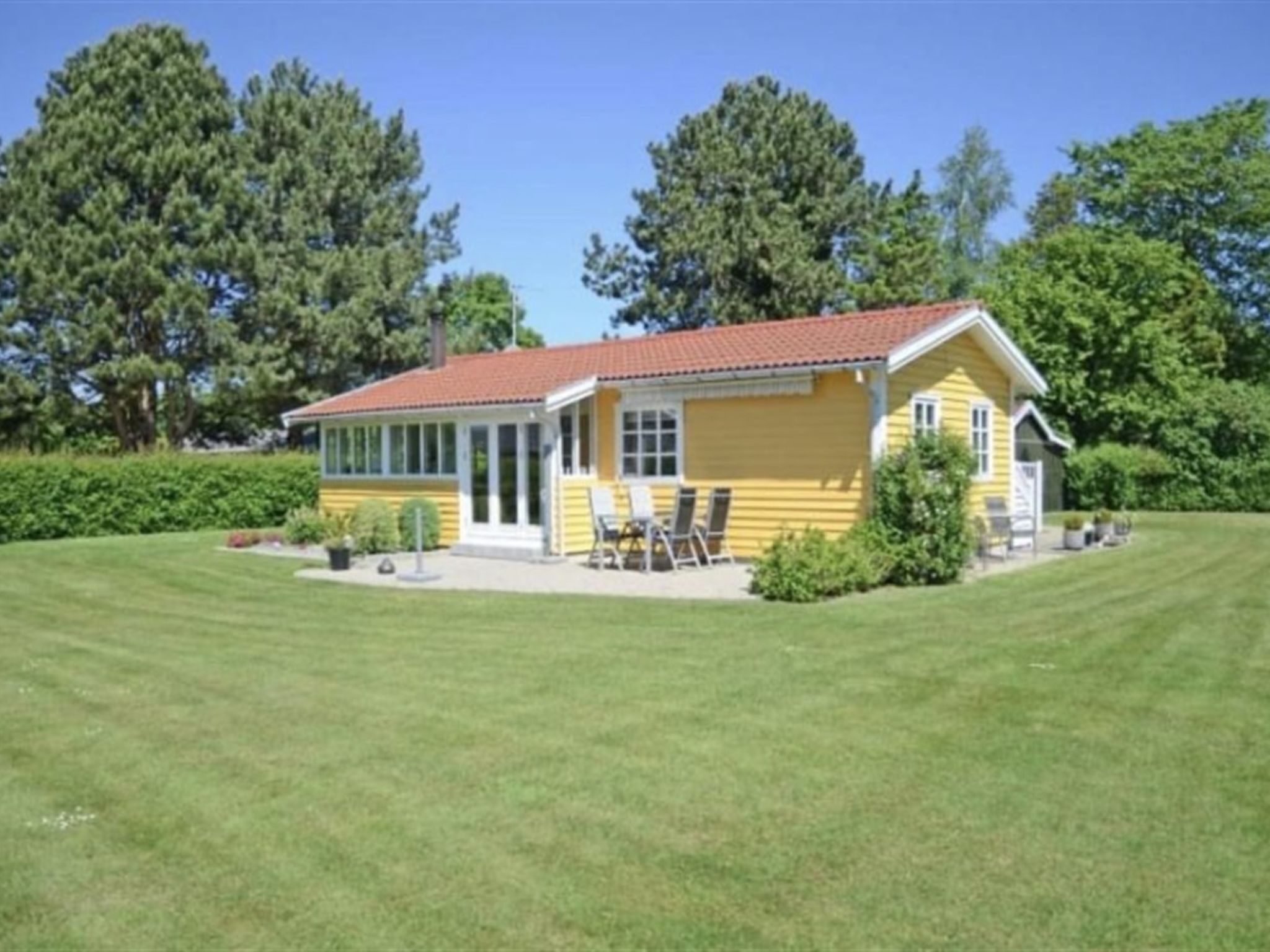A yellow house with a red roof, surrounded by a well-maintained lawn and trees.