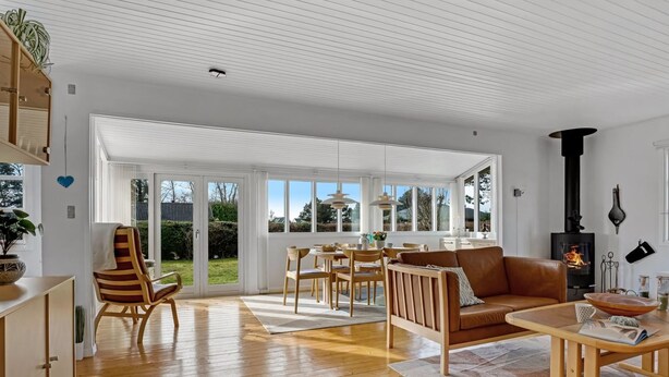 A spacious living room with a wooden floor, a fireplace, and a dining area with natural light from large windows. - "Andrine" - 100m from the sea by Interhome (Nakskov)