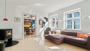 Un salon moderne avec une cheminée, un canapé et un coin repas visible à travers une porte ouverte.