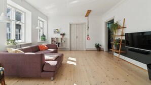 Un salon moderne avec un canapé, un téléviseur, un plancher en bois et de grandes fenêtres.