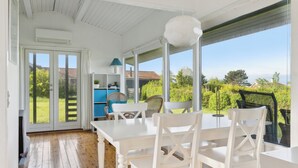 A bright room with a wooden floor, white furniture, and large windows offering a view of greenery and buildings. - Sea view, 200m to the beach, beautiful nature (Slagelse)