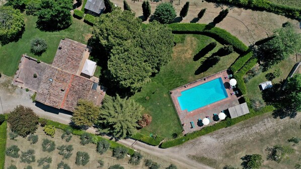Eine Luftaufnahme eines Anwesens mit Swimmingpool, einem großen Haus mit Ziegeldach und umliegender Bepflanzung.