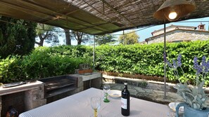 Eine Terrasse im Freien mit Grill, Tisch und einer Weinflasche.