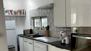 A modern kitchen with white cabinets, a built-in dishwasher, a coffee machine, and a window with a view of greenery. - Le cabanon du Cannet.charming, fully-equipped two-room apartment close to amenities. (Le Cannet)