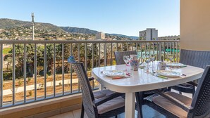 Een balkon met een eettafel, met uitzicht op een stadsgezicht en bergen in de verte.