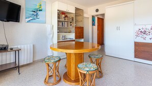Een eetgedeelte met een ronde houten tafel en vier krukken, een boekenkast, een televisie en een deur naar een andere kamer.