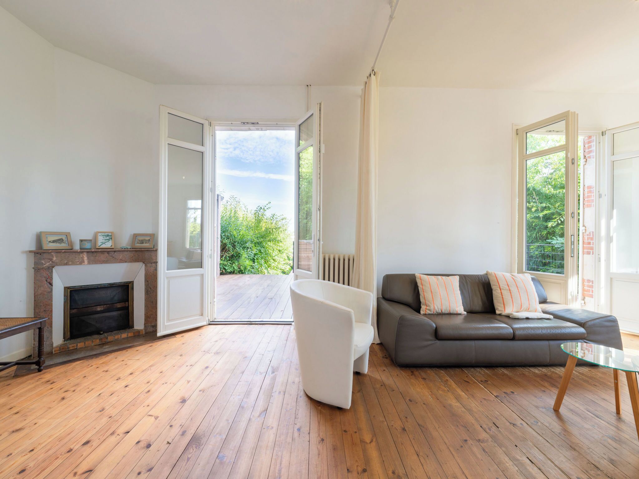 Un salon moderne avec une cheminée, un canapé, une table basse en verre et une vue sur la verdure grâce à des portes ouvertes.