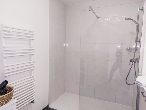 A shower area with a glass door, a white towel rack, and a basket with toiletries.
