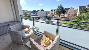 Un balcon agrémenté de meubles en osier, d’une table en verre et offrant une vue sur une rivière et des immeubles d’habitation.