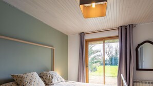 A bedroom with a large bed, a wooden headboard, a window with curtains, and a radiator. - Feliz Breizh by Interhome (Plounevez Lochrist)