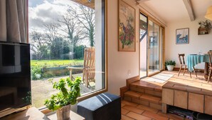 A spacious living area with a large window, a flat-screen TV, a wooden bench, and a dining table with chairs. - Feliz Breizh by Interhome (Plounevez Lochrist)