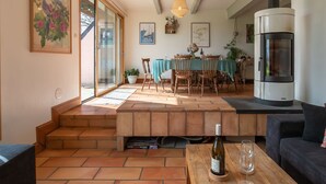 A cozy living room with a fireplace, a dining area with a table and chairs, and a staircase leading to an upper floor. - Feliz Breizh by Interhome (Plounevez Lochrist)