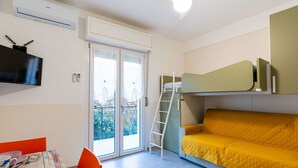 Une chambre compacte équipée d’un lit superposé, d’un ventilateur de plafond, d’un téléviseur à écran plat et d’une porte-fenêtre coulissante donnant sur un balcon.