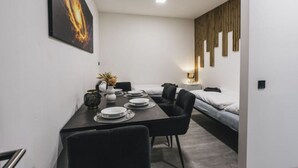 A modern hotel room with a dining area, a bed, and a wall-mounted light fixture.