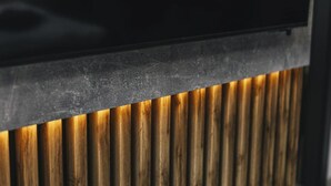 A close-up of a modern, dark-colored wall with a textured surface and a warm, illuminated panel below.