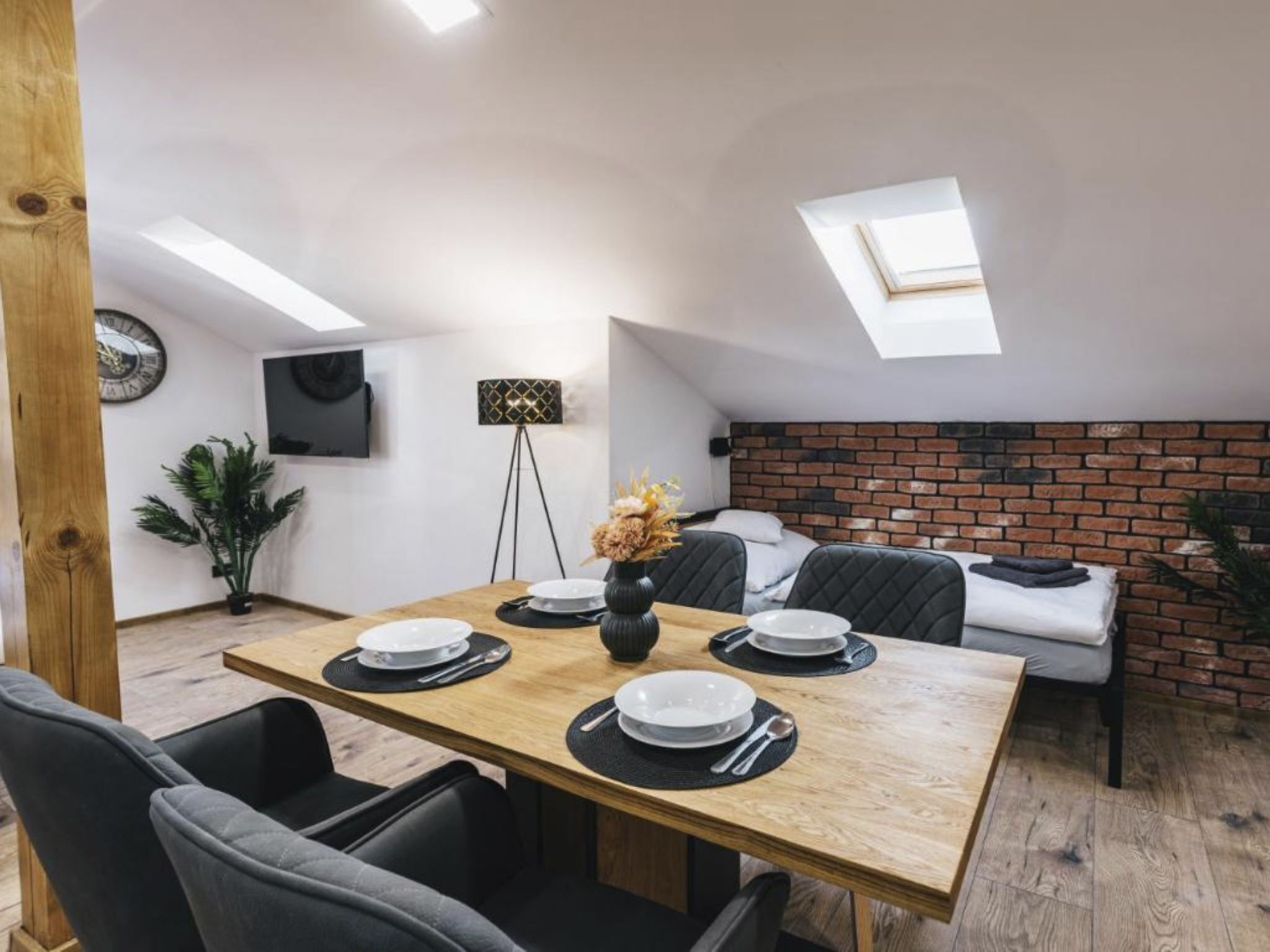 Een eetgedeelte met een houten tafel voor vier personen, zwarte stoelen, een bakstenen muur en een dakraam.