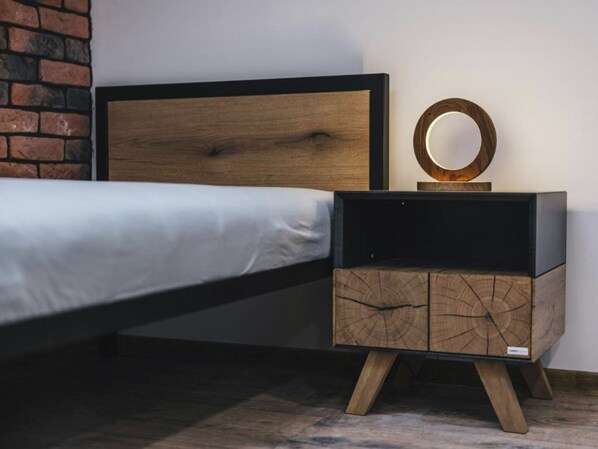 Una cama con cabecera de madera, una mesita de noche con espejo circular y un buró con detalles de madera.