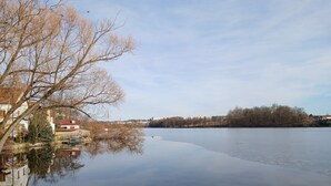 A calm lake with buildings on the left and trees in the background.
