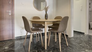 A dining area with a round table, four chairs, a round mirror, and a vase with dried plants. - Phaedrus Living: Koukaki Verdant Marble (Athina)