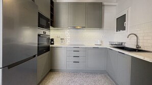A compact kitchen with a stainless steel refrigerator, a microwave, a kettle, a toaster, and a sink with a modern faucet. - Phaedrus Living: Koukaki Verdant Marble (Athina)