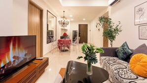 A modern living room with a flat-screen TV, a sofa, a coffee table, and a dining area with a red tablecloth. - SOHO Premier Residence (Ho Chi Minh City)