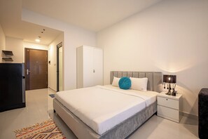 Ein modernes Hotelzimmer mit einem großen Bett, einem Nachttisch mit Lampe, einem Kleiderschrank und einem kleinen Schreibtisch.