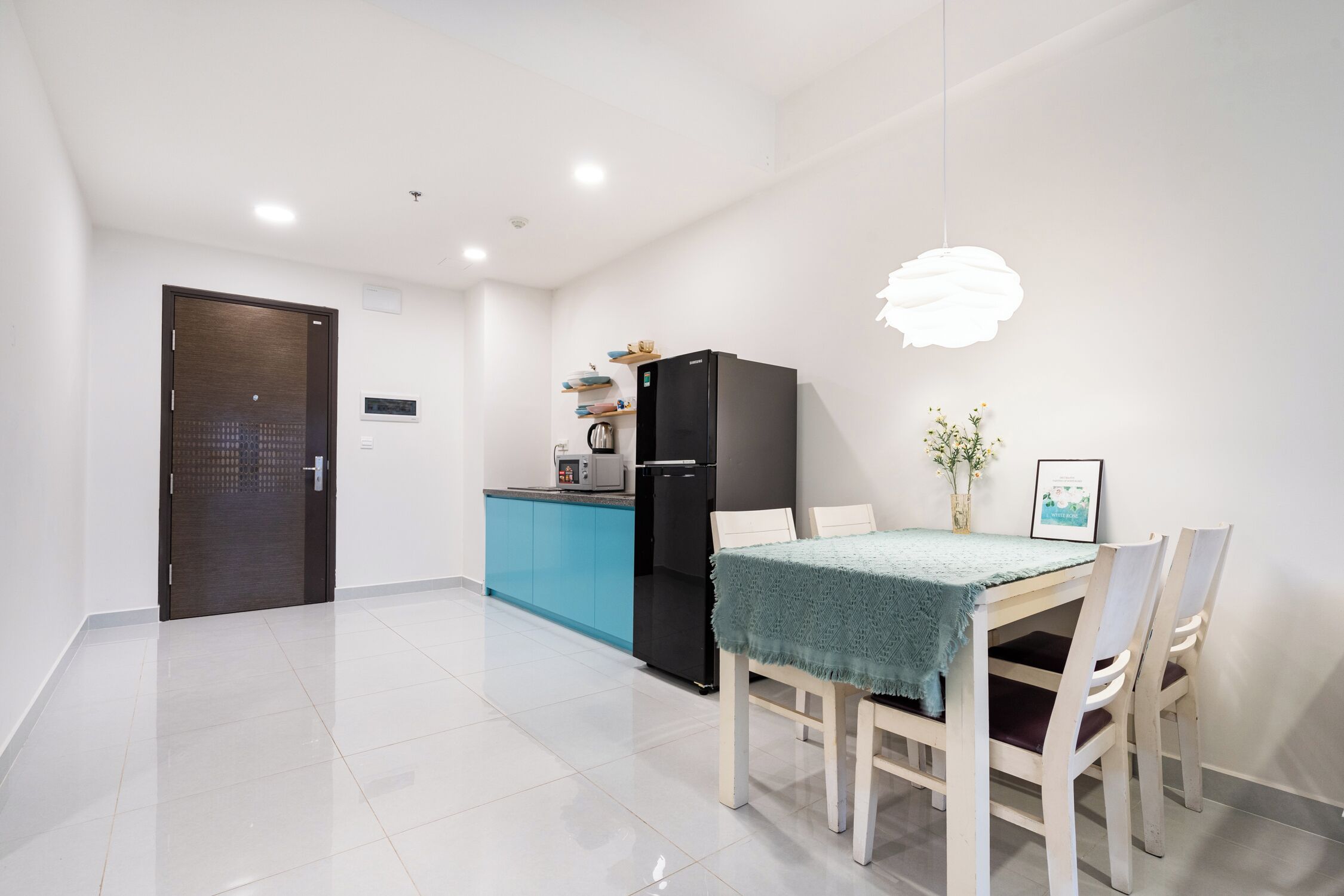 Une cuisine moderne avec un réfrigérateur noir, un plan de travail bleu et un coin repas comprenant une table et des chaises.
