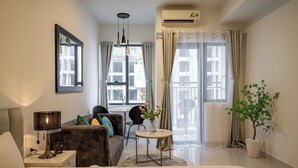 A modern hotel room with a bed, a sofa, a small table with a vase of flowers, a desk with a lamp, and a potted plant. - SOHO Premier Residence (Ho Chi Minh City)