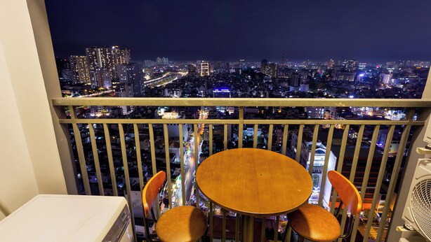 A balcony with a table and chairs, overlooking a cityscape at night. - SOHO Premier Residence (Ho Chi Minh City)