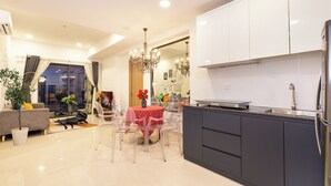 A modern kitchen with dark cabinets, a stainless steel refrigerator, and a dining area with a red tablecloth. - SOHO Premier Residence (Ho Chi Minh City)