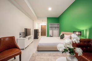 Ein modernes Schlafzimmer mit einem großen Bett, einem Fernseher, einer weißen Kommode und einer grünen Wand.