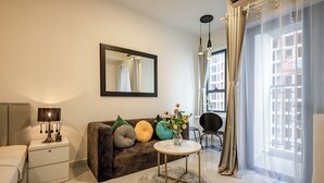 A modern living room with a sofa, a round coffee table, a side table with a lamp, a mirror, and a large window with curtains. - SOHO Premier Residence (Ho Chi Minh City)