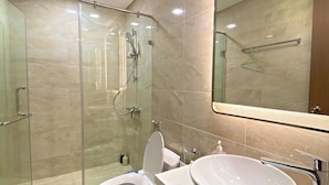 Un baño moderno con ducha envuelta en vidrio, inodoro y un lavamanos grande con espejo arriba.