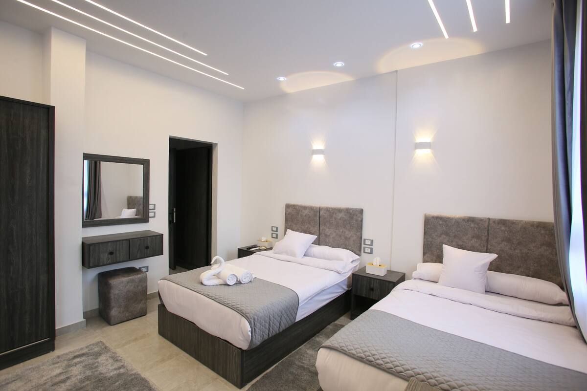 Una habitación de hotel moderna con una cama grande, mesitas de noche, un espejo y un armario.