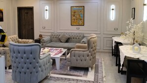 Een moderne woonkamer met een hoekbank, gestoffeerde fauteuils, een salontafel en een kroonluchter.
