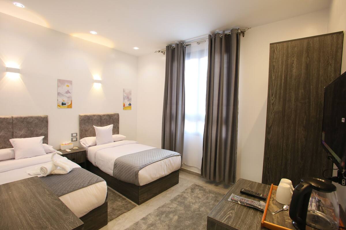 Habitación de hotel con dos camas, televisor, cafetera y bandeja con un control remoto.