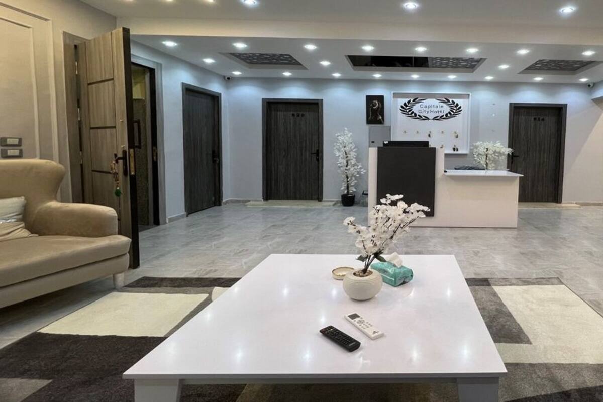 Zona de recepción de un hotel con un mostrador blanco, un sofá y una mesa de centro con un jarrón y un control remoto.