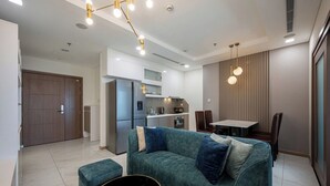 A modern living room with a teal sofa, a dining table, and a kitchen in the background. - DE LA SOL Centre Point By An Gia Hospitality (Ho Chi Minh City)