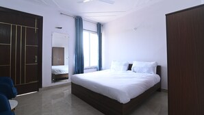 A bedroom with a bed, a wardrobe, a ceiling fan, and a window with curtains. - Ima Retreat (New Delhi)
