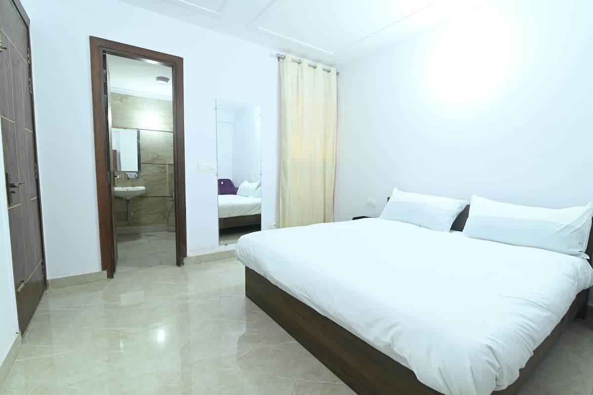 A bedroom with a large bed, a wooden door, a bathroom with a sink, and a mirror.