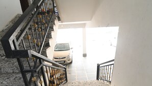 A marble staircase with a black metal railing leading to a car parked in a garage. - Ima Retreat (New Delhi)