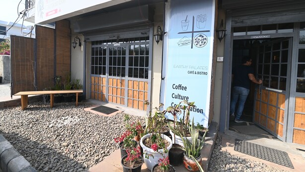 A cafe with a sign reading "Earthy Palates Cafe & Bistro" and a man entering through the door. - Ima Retreat (New Delhi)