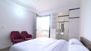 A hotel room with a bed, two red chairs, a wardrobe, and a balcony. - Ima Retreat (New Delhi)
